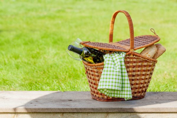 Picnic basket with wine and baguette on garden sunny grass.